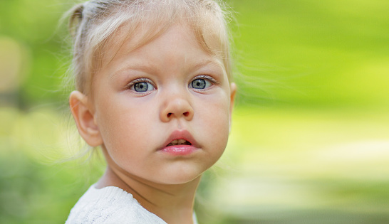 Portrait of serious beautiful little girl of 2 years looking at camera on the green blurred background with copy space