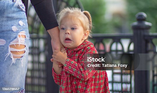 istock Caucasian little girl of 2 years with scared face holding hand of mother in summertime 1360218557
