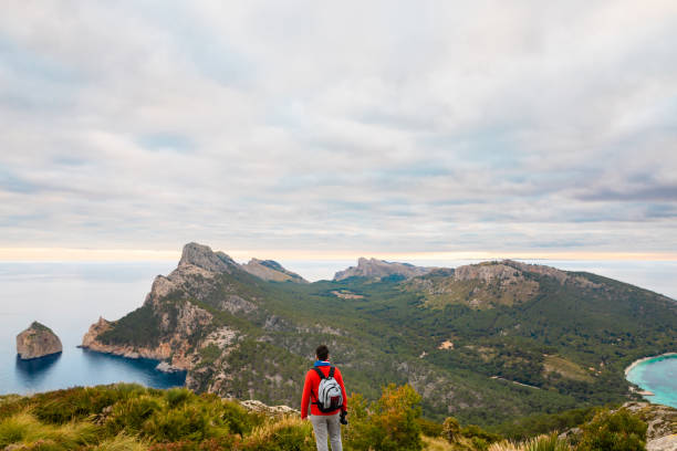 istock Young hiker from behind looking into the distance with binoculars in his hands in front of a stunning landscape on the north coast of Mallorca 1360219749