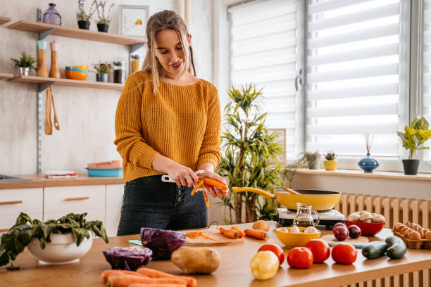 istock Young Woman Peeling Off Carrots In The Kitchen 1360219957