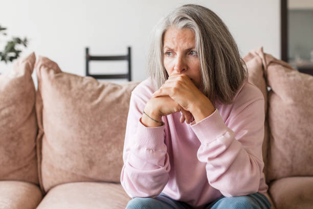 istock Sad pensive middle age woman looking down depressed sitting on the sofa 1360220815