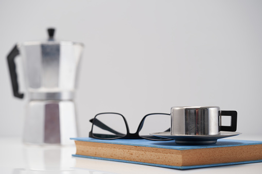 eyeglasses and hard cover book with cup of coffee and moka pot