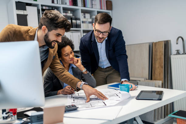 Small multiracial group of business people reviewing some blueprints at the office desk stock photo