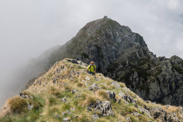 istock Young hiker clambering up grassy ridge, mountain top 1360224582