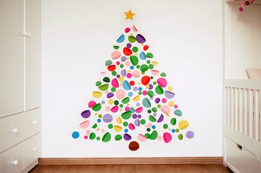 Idea of a Christmas tree with your own hands is hand made of multicolored paper and colored cardboard glued on the wall of the nursery. Children's bedroom interior. Color circles with Very Peri. Xmas