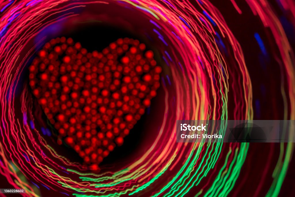 Glittering red heart inside the glowing multi colored circles Glittering red heart inside the glowing multi colored circles on a dark background. Love - Emotion Stock Photo