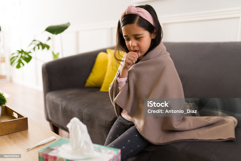 Sad child suffering from the flu Suffering little girl with a bad cold or seasonal flu. Beautiful kid coughing while wrapped in a blanket Child Stock Photo