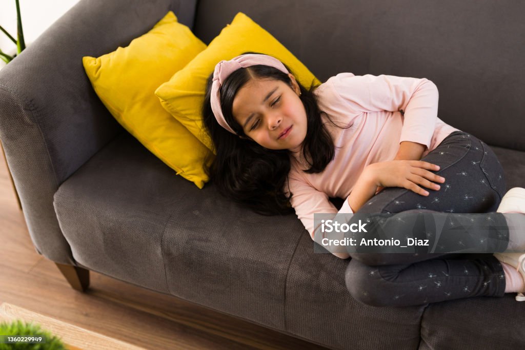 Sad little child with a stomach virus Sick elementary girl suffering from a stomach ache. Hispanic girl suffering from abdominal pain Stomachache Stock Photo
