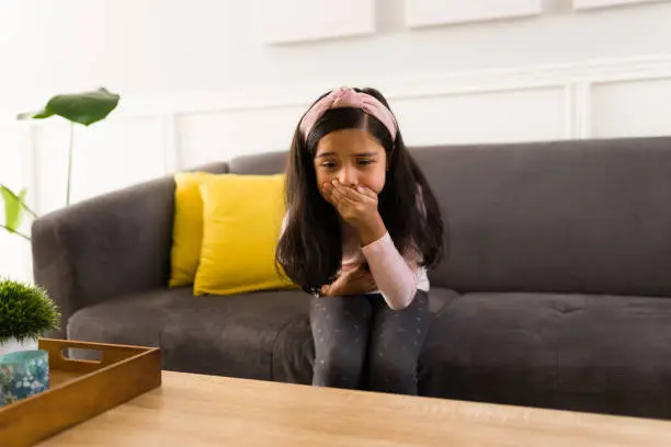 Hispanic girl feels ill and covering her mouth because of the nausea. Little girl suffering from stomach ache wants to vomit