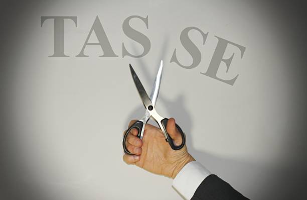 forbici a mano che tagliano la parola "tasse" che traduce in italiano tasse, concetto di riduzione della tassazione in italia. - libertarian foto e immagini stock