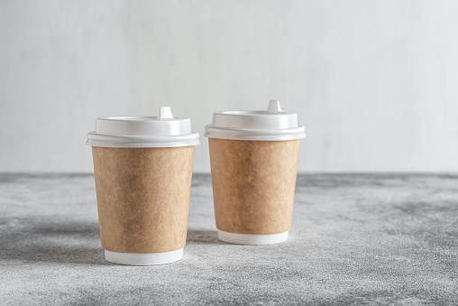 Paper cup for coffee on a gray concrete grunge background. Side view, selective focus. Disposable tableware