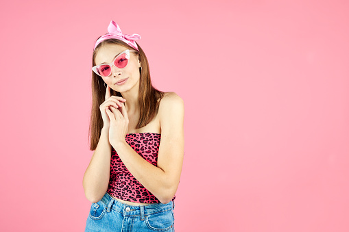 Cool hipster girl wearing stylish glasses. Positive young woman looking at camera on pink background. Caucasian female university student posing.Casual style with beauty accessories
