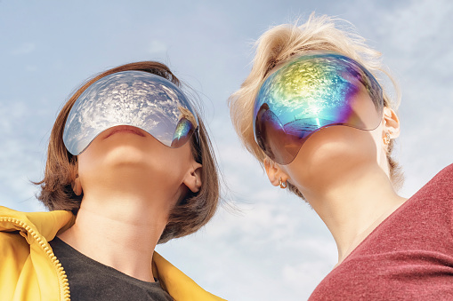 two young women in mirrored masks that completely cover their faces looking forward. Low angle view