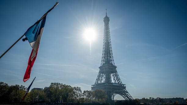 istock Eiffel Tower with French flag flying in blue sky. 1360244446