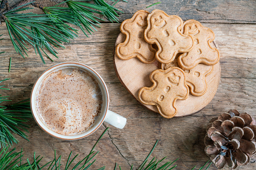 Christmas cookies, Cappuccino or Latte coffee and gingerbread man cookies on wooden table decorated with pine tree branches for noel or new year. Man shaped noel biscuits