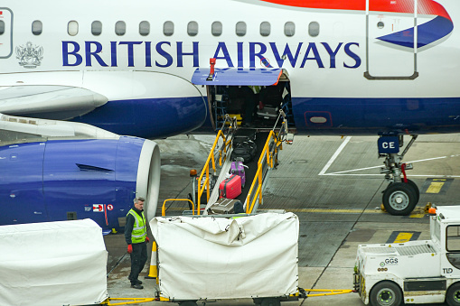 London, England - April 2019: Suitcases being unloaded from a British Airways jet at Gatwick Airport's South terminal building