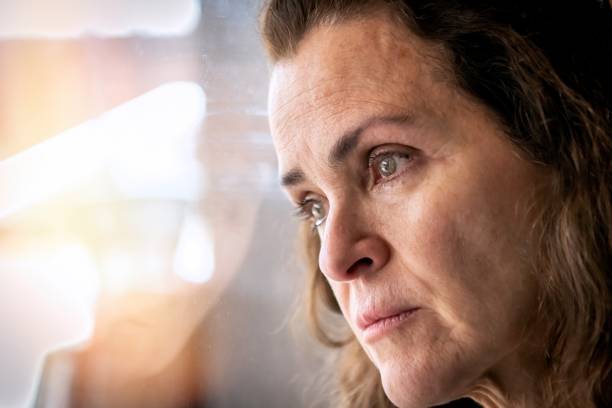 istock Concerned mature woman looking through a window 1360247111