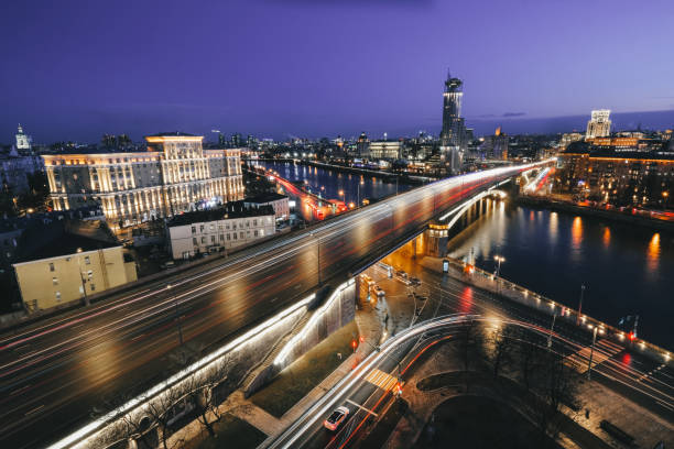 View on the Krasnokholmsky Bridge over the Moscow River. The sun goes down, cars move across the bridge, leaving headlights.
