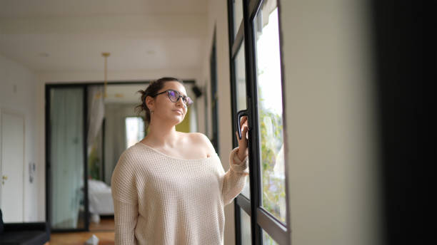 istock Young woman looking through window at home 1360247387