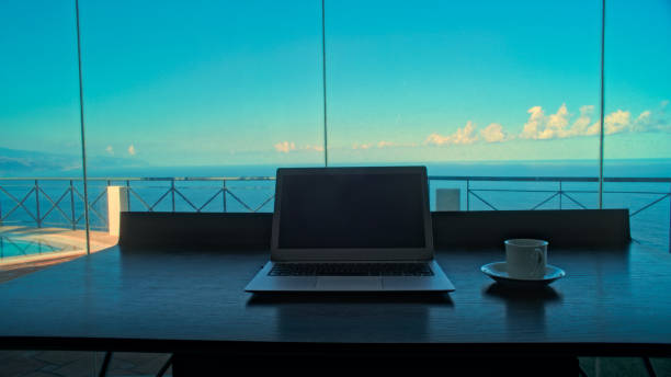 istock Empty desk with a view and laptop. Cozy room ready for office work. Windows with sea panorama 1360248263