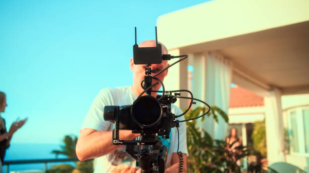 istock Session on a patio. Man in background posing for a photo. Photographer setting camera 1360249885