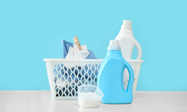 istock Detergents and children's clothes on white table near light blue wall. Space for text 1360250358