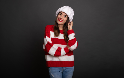 Close up portrait of a beautiful smiling stylish woman in white winter hat while she posing and having fun isolated on gray background