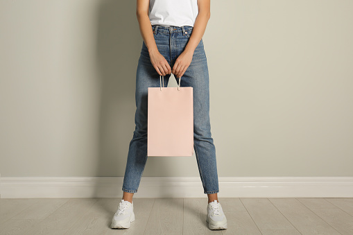 Woman with paper shopping bag near light grey wall, closeup