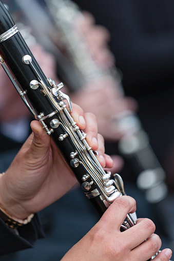 Daytime sideview close-up of a clarinet being played by a female amateur musician in an orchestra at a free outdoor concert - shallow DOF, other clarinets in the background are out of focus