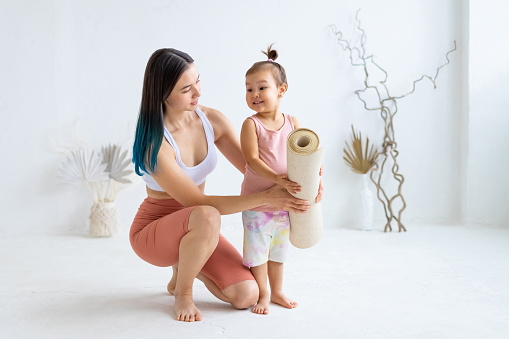 Young mom with little daughter hold yoga mat before practice. Healthy parenting.
