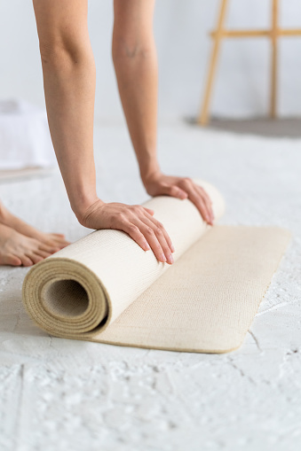 Close-up of female hands rolling out beige yoga mat. Yoga Home.