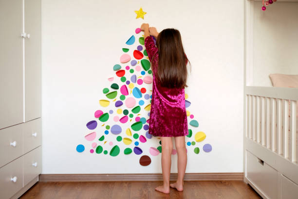 istock Girl decorates the wall with multicolored circles forming a Christmas tree. 1360262034
