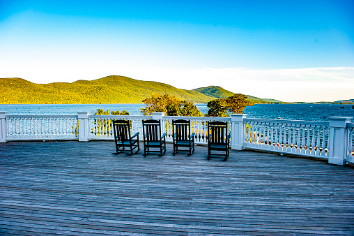 A set of rocking chairs on a balcony overlooking Lake George, NY.  Lake George is a town in New York’s vast, protected Adirondack region of mountains and old-growth forest. The town sits on the lake of the same name.