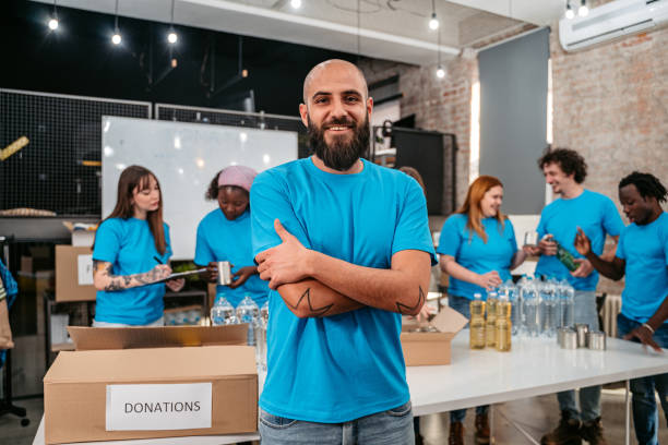 Proud volunteer standing in front of friends working in donation center Portrait of proud young beautiful male volunteer standing in front of friends who are working in donation center. community center food stock pictures, royalty-free photos & images