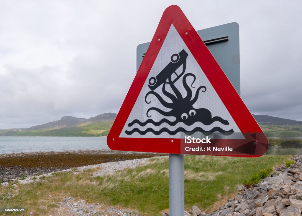 Humorous Scottish road sign A humorous road sign beside a causeway near the coastal village of Tongue in the northwest of Scotland.  The warning sign notifies drivers that they are going to be driving close to the sea. The black and white illustration is of an octopus holding an upturned car in its tentacles. Road Sign Stock Photo