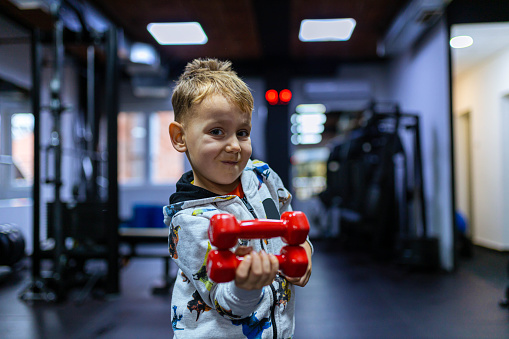 Curious little boy, playing at the gym, with small dumbbells