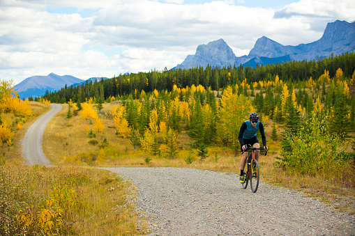 A man goes for a gravel road bike ride at the Canmore Nordic Centre in Alberta, Canada. Gravel bicycles are similar to cyclo-cross bikes with larger tires for riding on rough terrain.