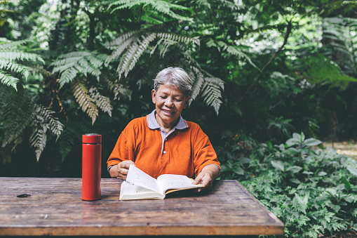 asian senior adult taking rest and reading book during jogging activity on the park