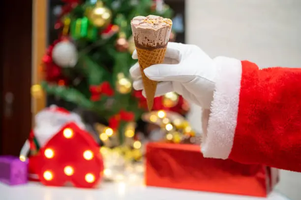 Santa Claus holding an ice cream cone in front of Christmas decorations at home