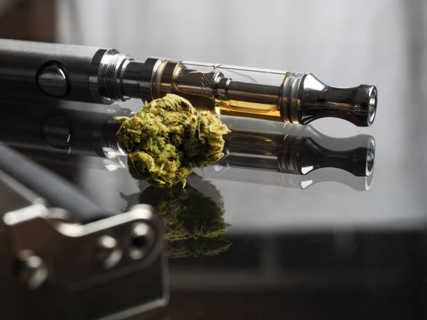 close up shot of real cannabis or weed with cannabis oil in cartridge of vape  pen in the background, roller blurred in foreground and text space on the right under the dark theme - vape stockfoto's en -beelden