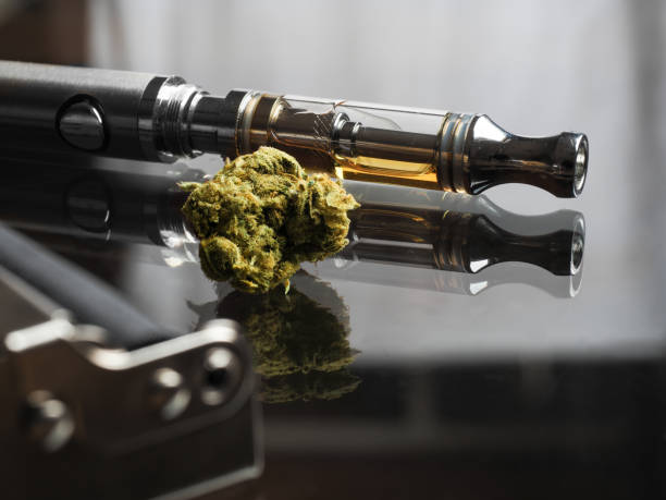 Close up shot of real cannabis or weed with cannabis oil in cartridge of vape  pen in the background, roller blurred in foreground and text space on the right under the dark theme Close up shot of real cannabis or weed with cannabis oil in cartridge of vape  pen in the background, roller blurred in foreground and text space on the right under the dark theme electronic cigarette stock pictures, royalty-free photos & images