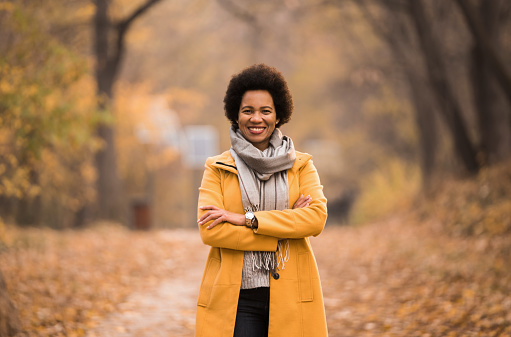 Happy African American woman looking at camera  with arms crossed while enjoying an autumn morning walk.