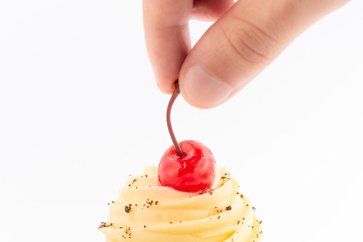 Hand putting a cherry on top of the muffin, on a white background with copy space.