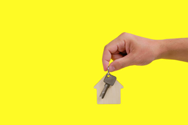 istock House keys with a keychain in hand on a yellow background. 1360299771