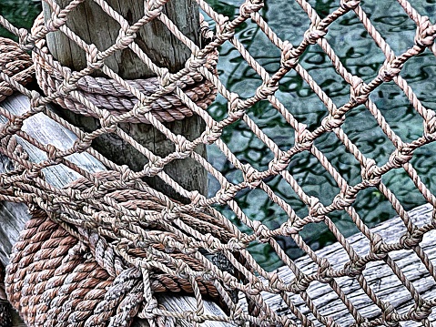 Rippled blue waters beneath heavy fishing nets along nautical 
style boardwalk in fishing village.
