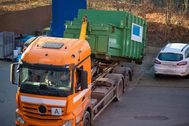 Photo of orange truck drops off a trash compactor in the yard of a hospital