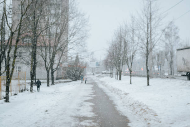 istock Defocus winter street, falling snow, day outdoors. Sidewalk, people and snowfall blurred backdrop 1360308925
