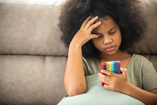 Little African child girl looking on mobile phone screen with sadness