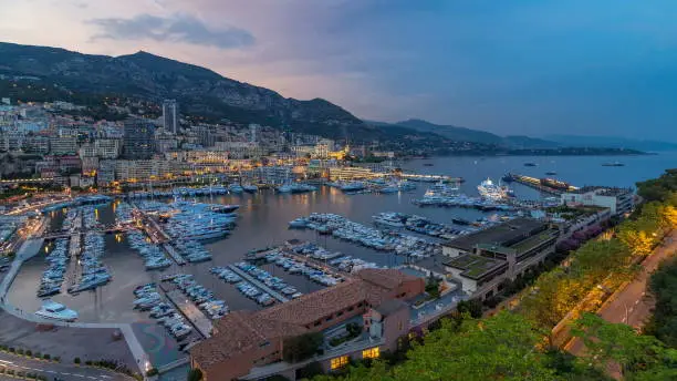 Panorama of Monte Carlo day to night transition timelapse from the observation deck in the village of Monaco with Port Hercules. Buildings with illumination and yachts in harbor aerial top view. Traffic on the road