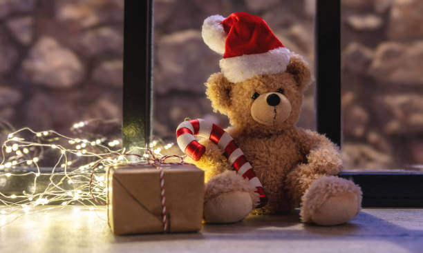 istock Wait for Santa. Teddy bear on a window sill. Christmas lights and gift box, warm home interior 1360319006